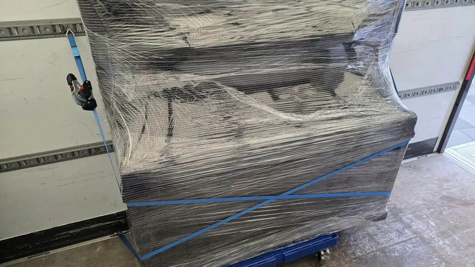 Vollständig in Folie verpacktes Pianino, mit Spanngurten auf dem Klavierschlitten gesichert