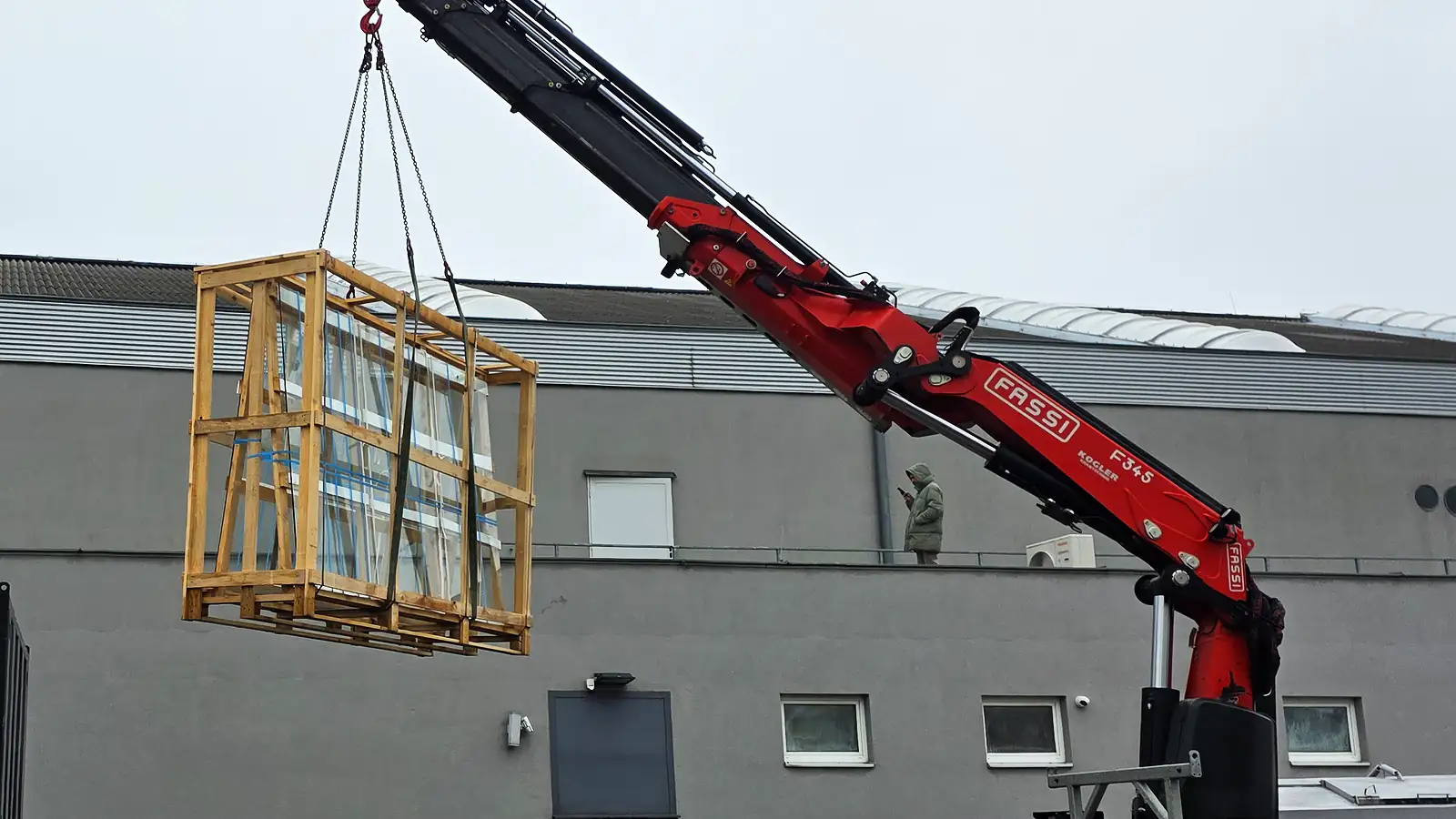 Autokran hebt eine Lattenkiste am Gehänge über eine Fassade — dieselbe Technik, wenn ein Flügel nicht durchs Stiegenhaus passt